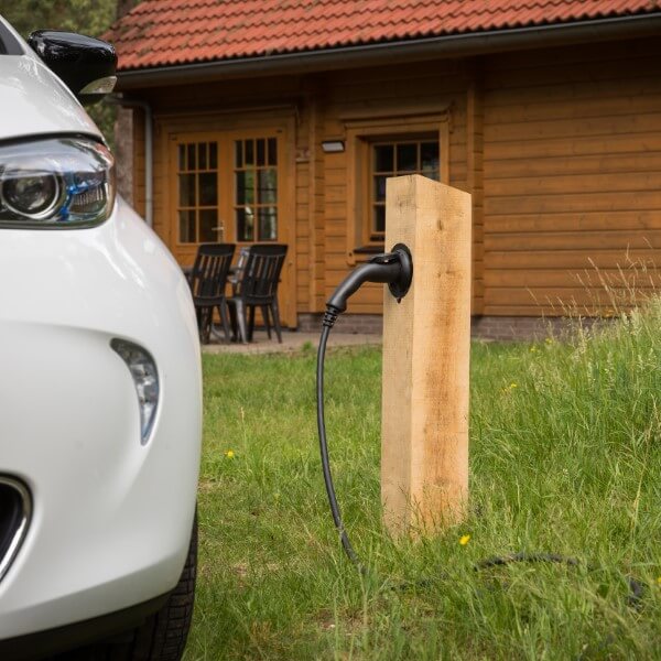 Houten oplaadpaal in het gras met elektrische auto voor een huisje